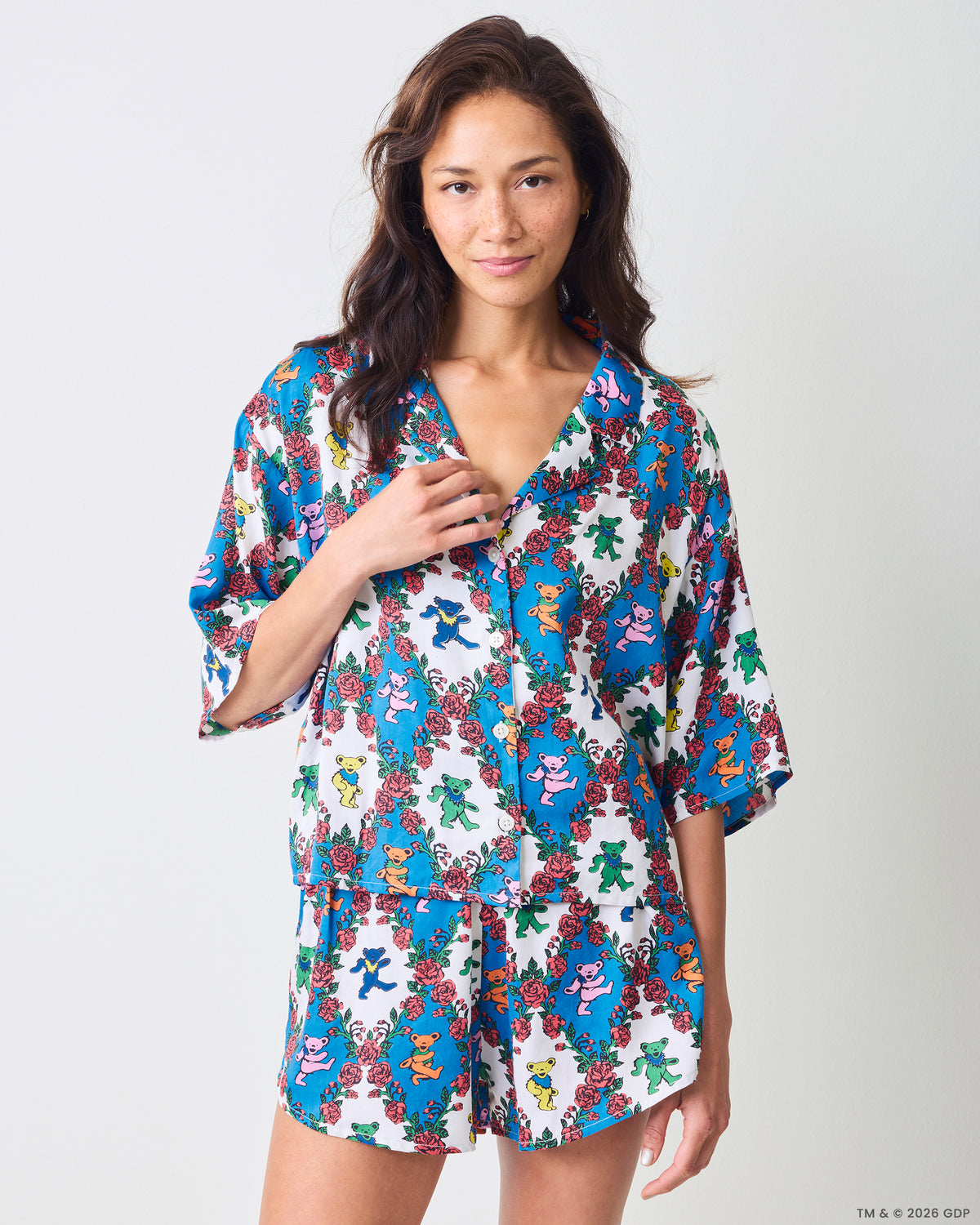 Person wearing a matching short-sleeve button-front top and shorts set with blue floral and colorful bear motifs.