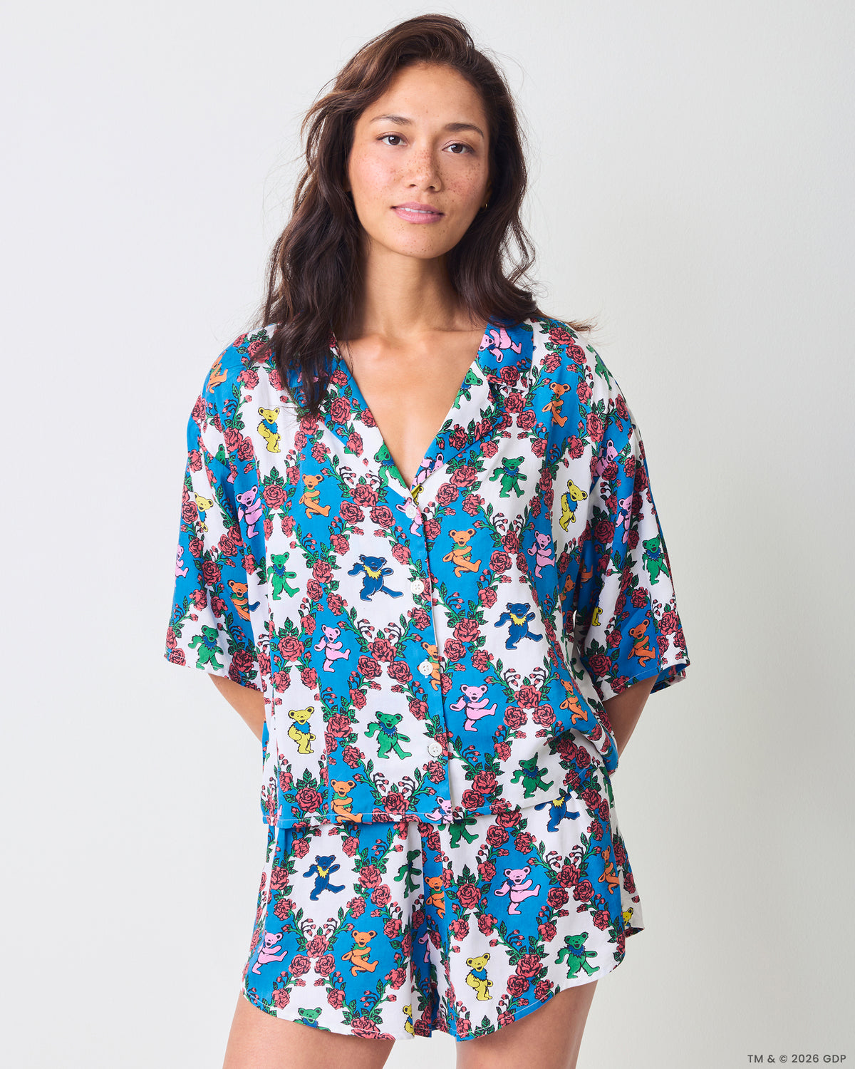 Front view of a person wearing a matching short-sleeve button-front top and shorts set with blue floral and colorful bear motifs.