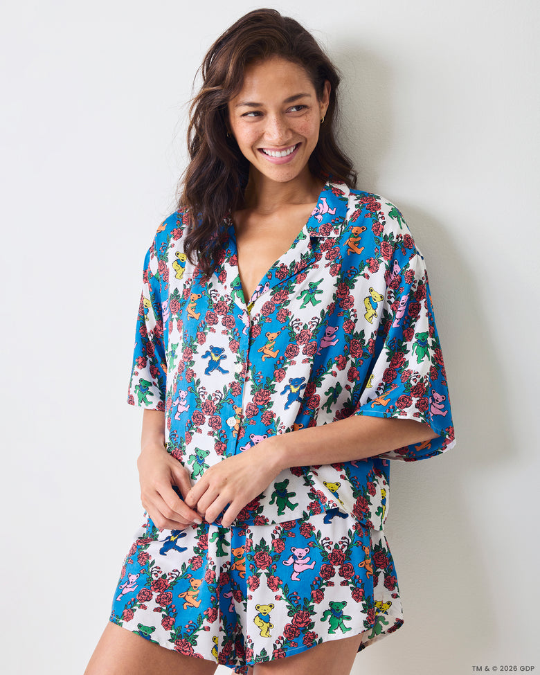 Front three-quarter view of a short-sleeve button-front top and matching shorts with a blue-and-white bear-and-rose print.