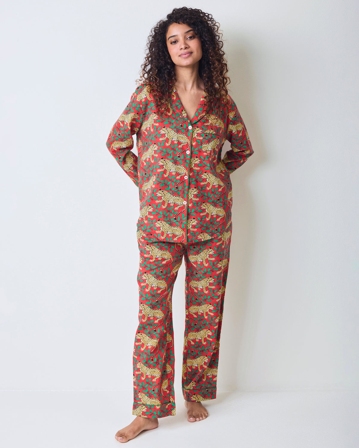 Person standing barefoot and wearing the red Winter Holly Bagheera button-front pajama top and matching long pants.