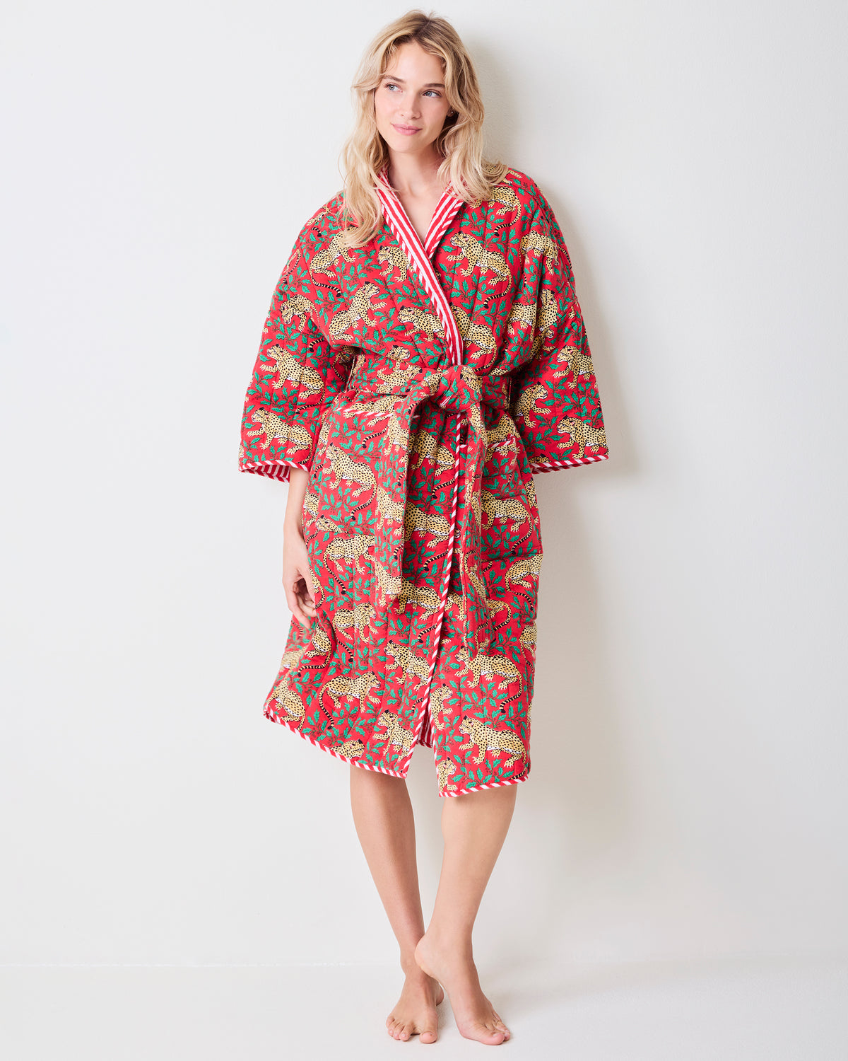 Full-length front view of a red reversible quilted robe with a leopard and green holly print, matching belt, and striped trim.