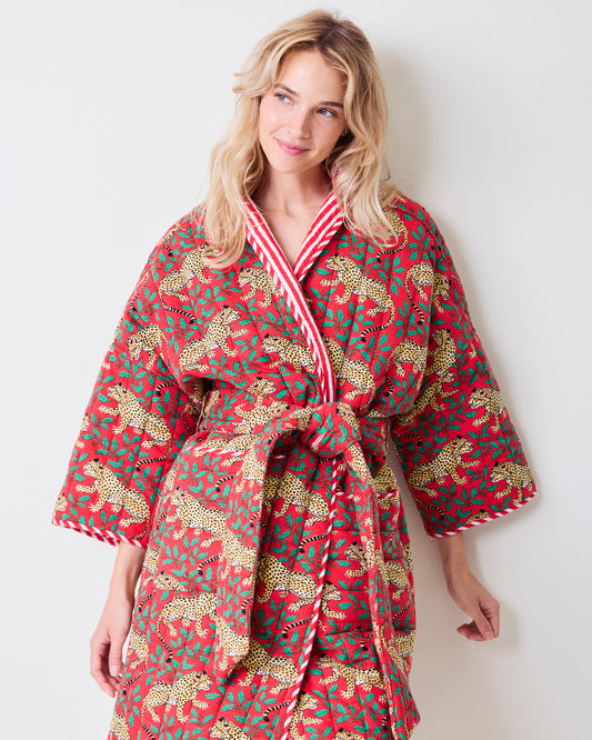 Front view of a red reversible quilted robe with leopard and green holly print, striped trim, matching belt, and pockets.