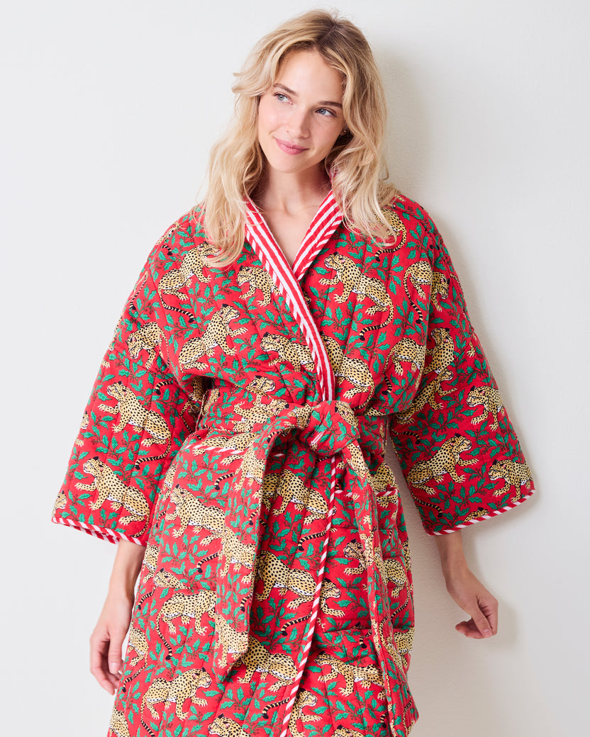 Front view of a red reversible quilted robe with leopard and green holly print, striped trim, matching belt, and pockets.
