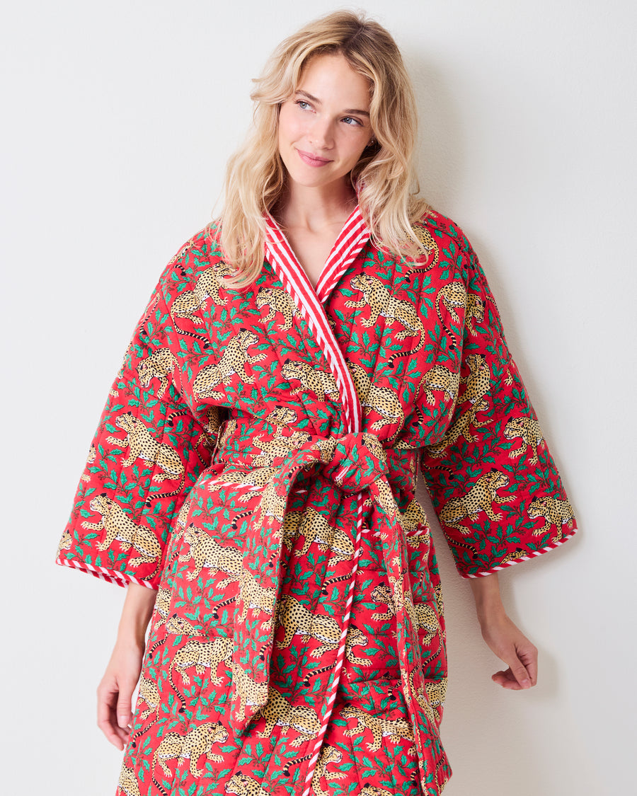 Front view of a red reversible quilted robe with leopard and green holly print, striped trim, matching belt, and pockets.