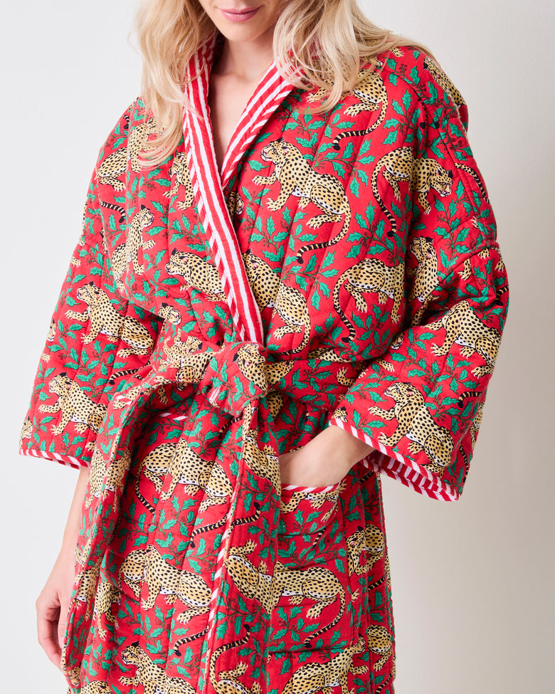 Close-up front view of a red reversible quilted robe showing the leopard and green holly print, striped trim, belt, and pocket.