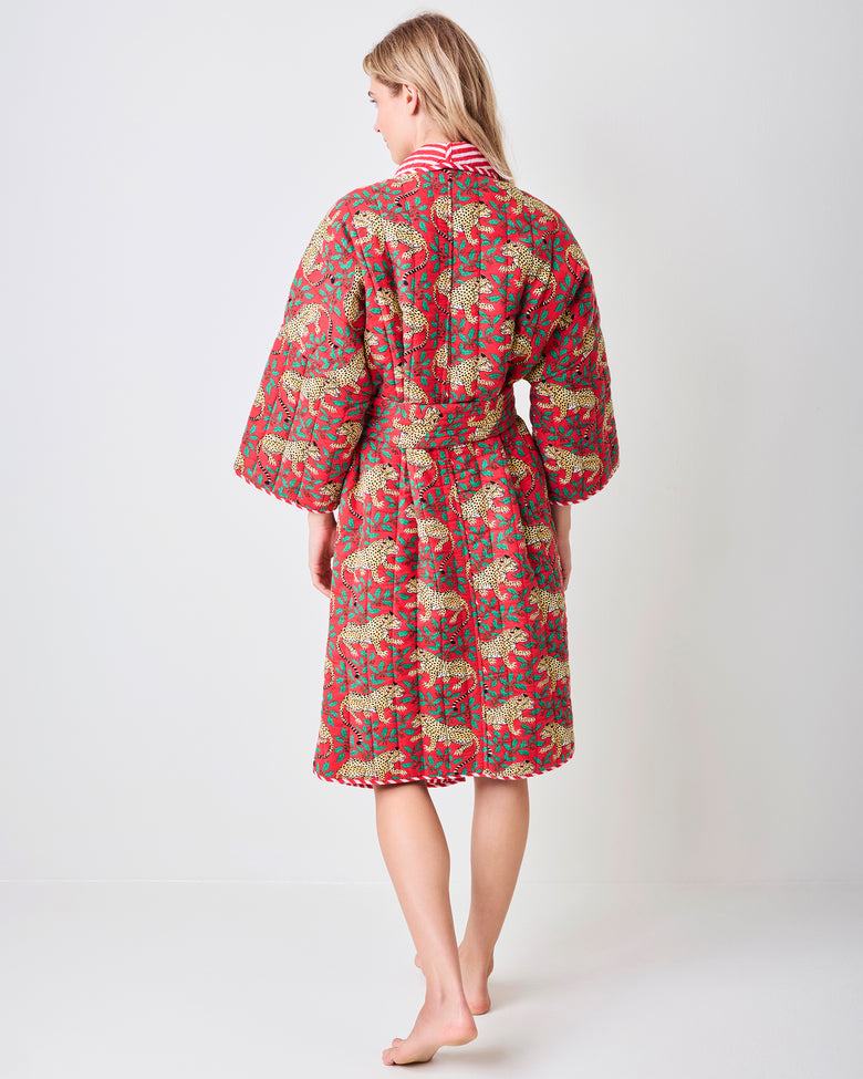 Back view of a red reversible quilted robe with a leopard and green holly print, matching belt, and striped collar trim.