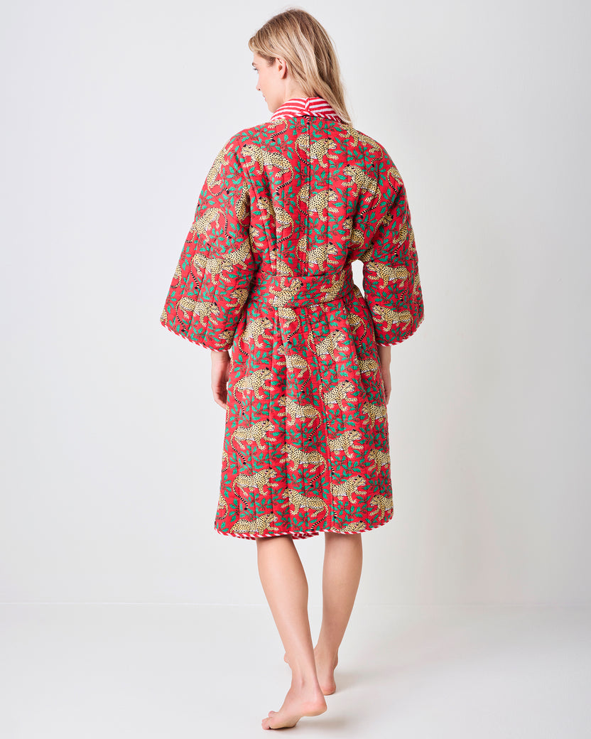 Back view of a red reversible quilted robe with a leopard and green holly print, matching belt, and striped collar trim.