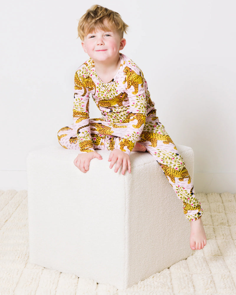Child seated on a white cube wearing a light-colored pajama set with a spotted cat pattern.