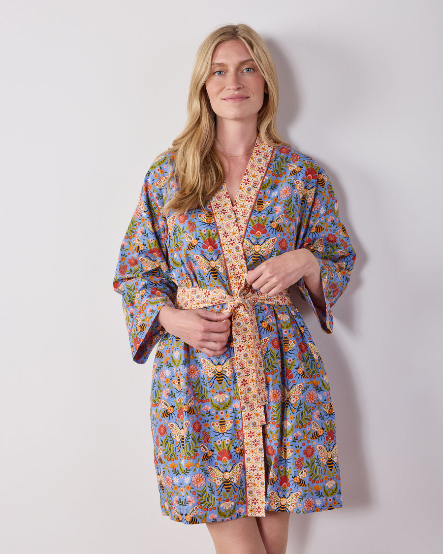 Front view of a person wearing the Delphinium Blue Bee Tapestry robe with a tied belt, long sleeves, and floral bee print.
