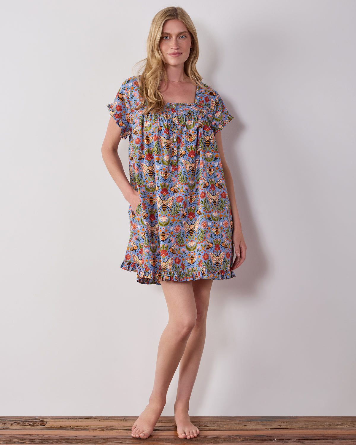 Model wearing the blue Bee Tapestry pintuck nightgown, shown from the front with short sleeves and a ruffled hem.
