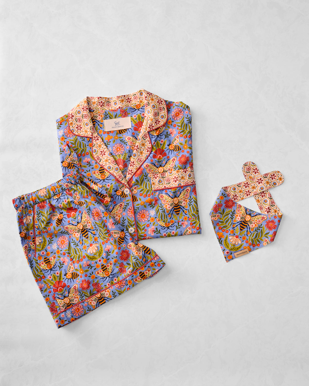 Flat lay of the Bee Tapestry short pajama set and pet bandana in Delphinium Blue, showing the button-front top, shorts, and matching bandana.