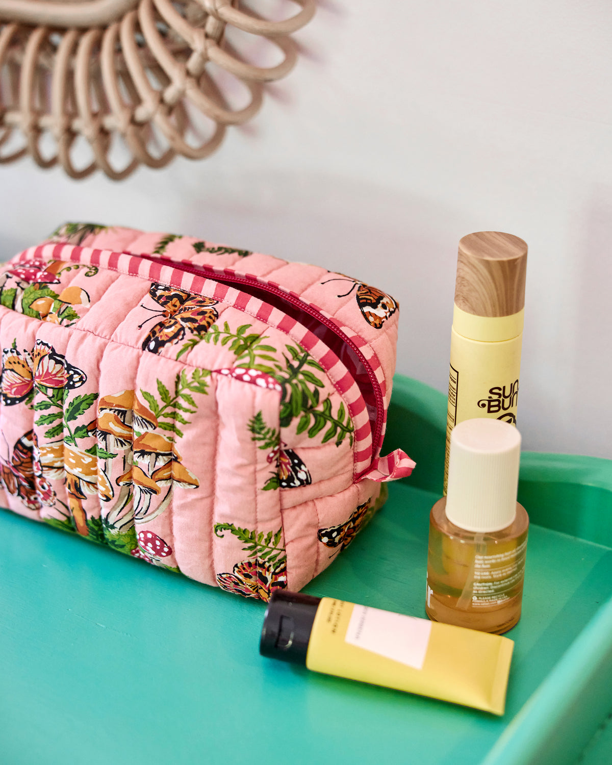 Pink quilted pouch with butterfly, mushroom, and fern print on a turquoise tray.
