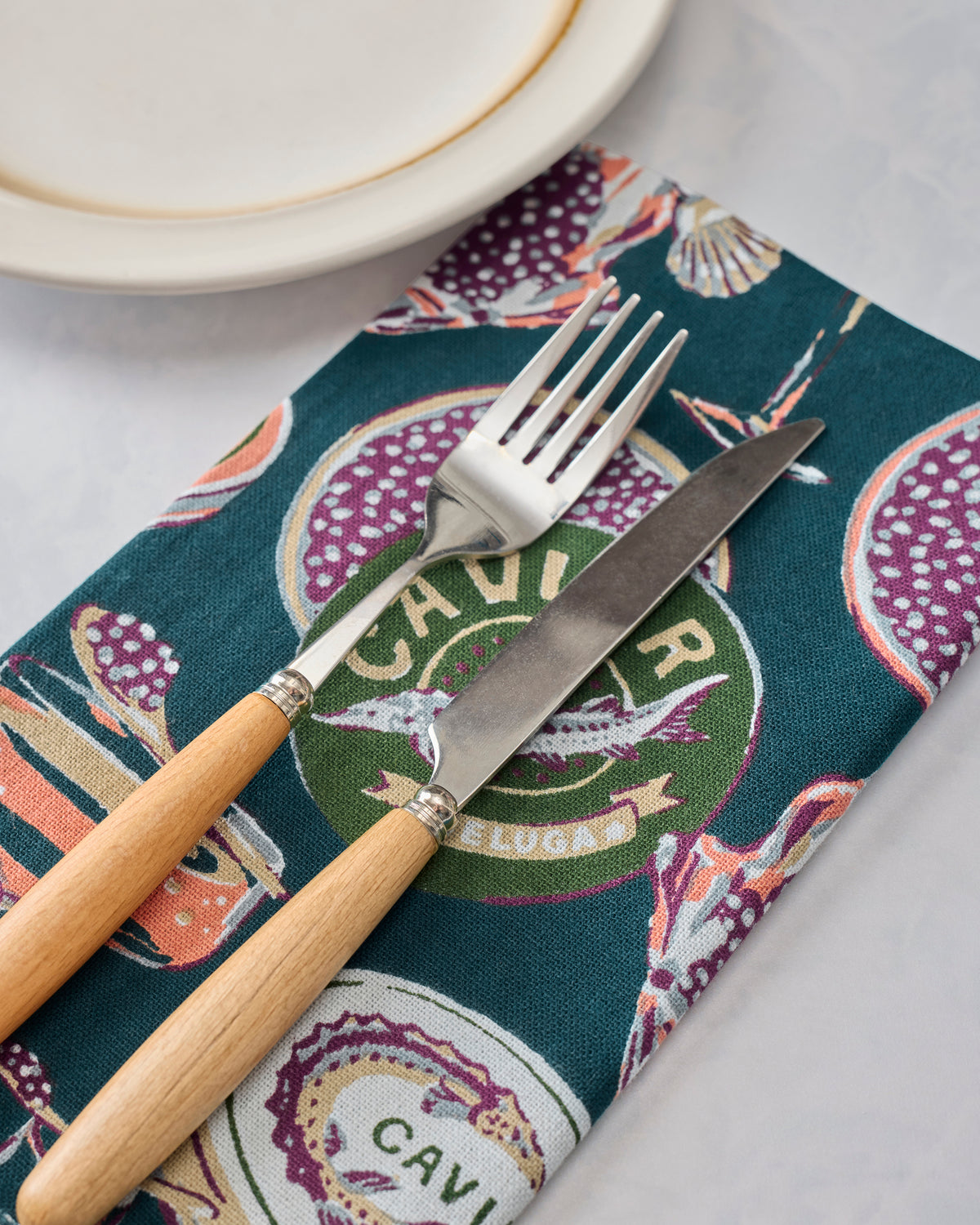 Champagne & Caviar dinner napkin styled with a white plate, fork, and knife.
