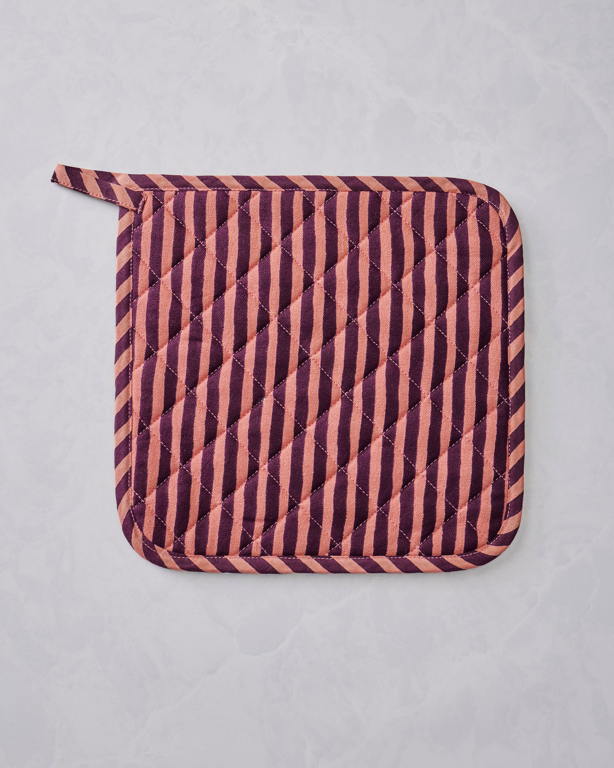 Quilted Champagne & Caviar pot holder with diagonal burgundy and peach stripes and rounded corners, shown flat.