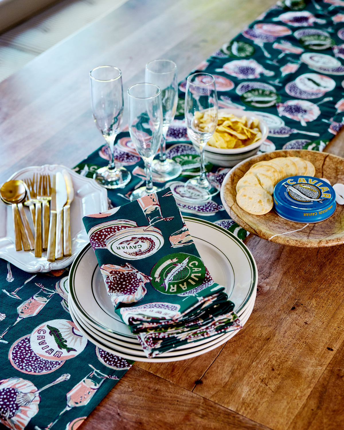 Champagne and Caviar table runner styled with plates, champagne flutes, cutlery, chips, crackers, and a caviar tin.