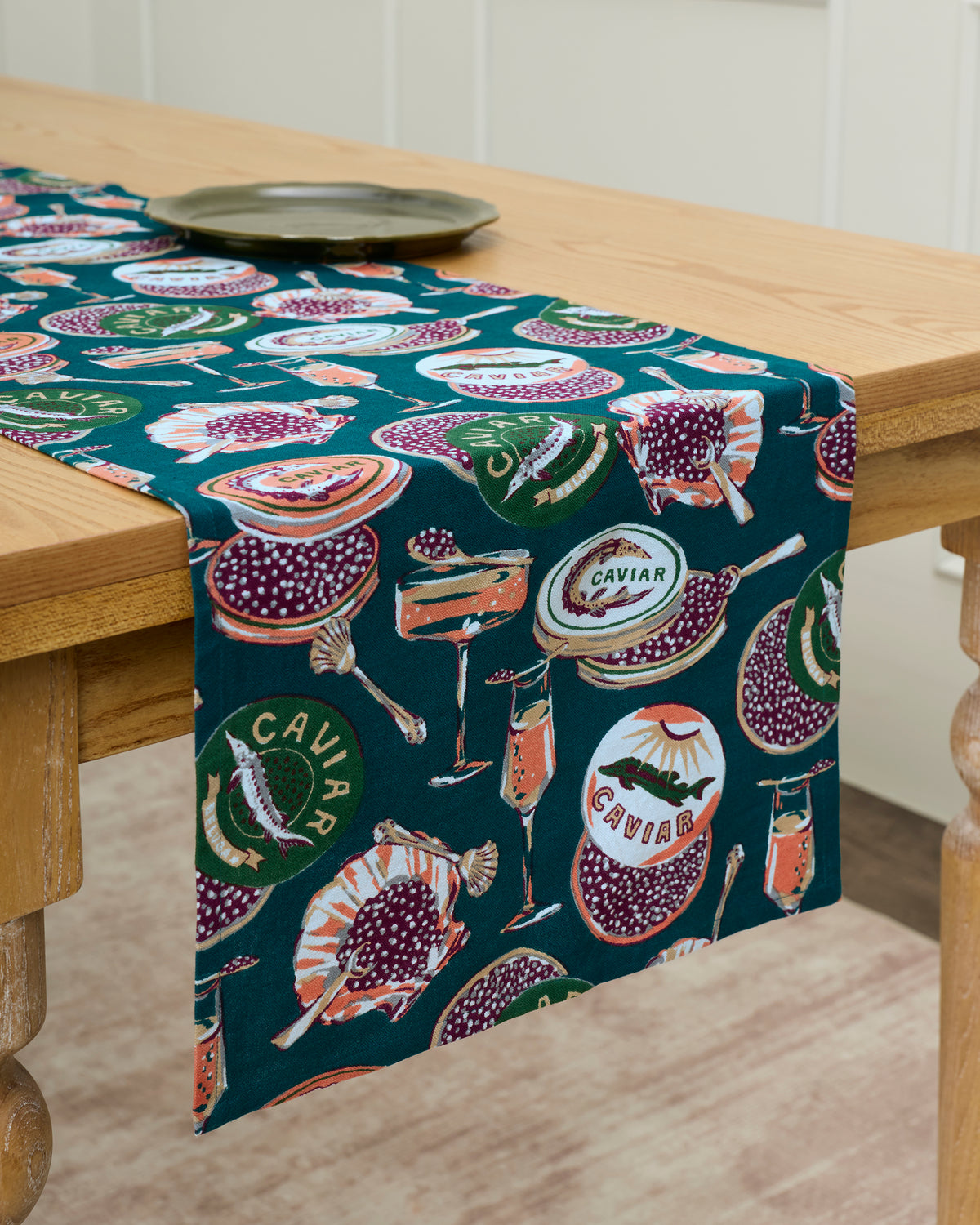 Champagne and caviar table runner draped over a wooden table, printed with caviar tins, seafood, and serving items.
