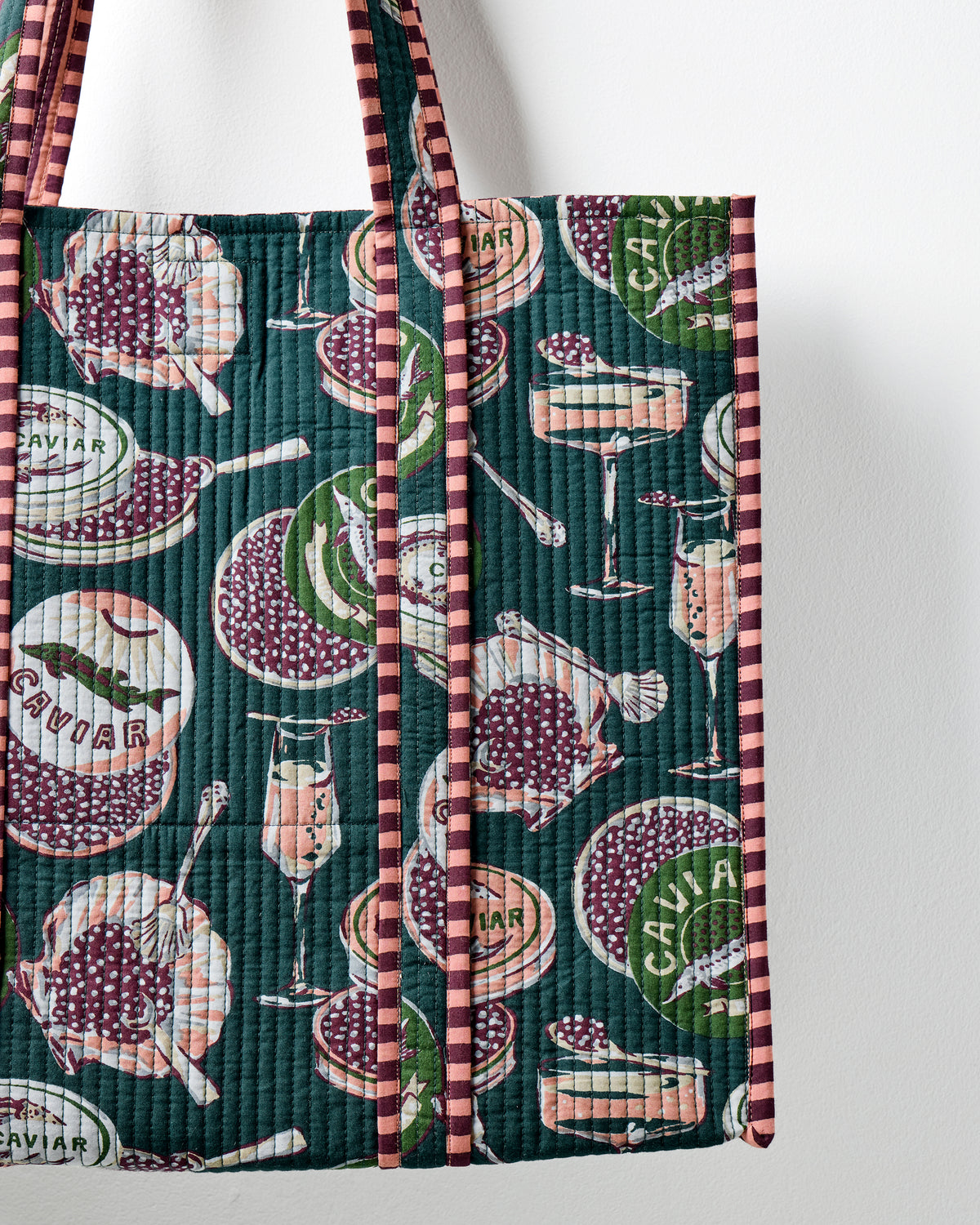 Close-up of the peacock-feather traveler tote showing its Champagne & Caviar print and striped edging.
