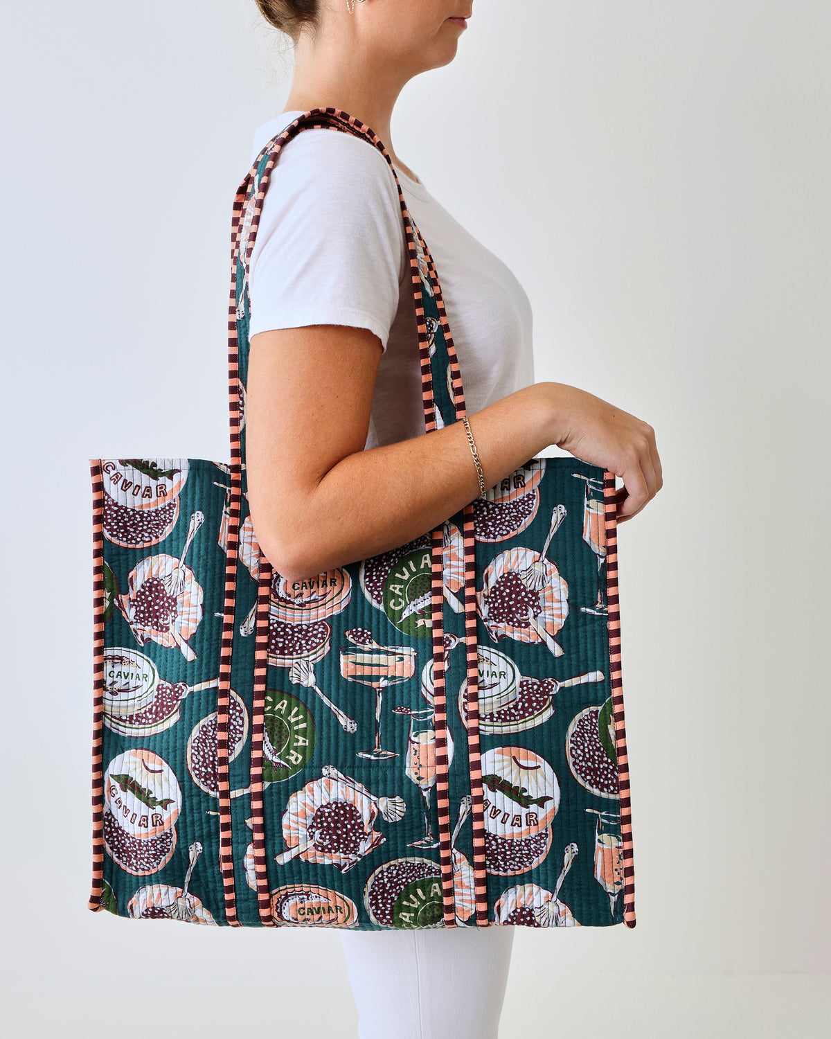 Front view of the Champagne & Caviar Traveler Tote with peacock-feather print, carried over a person’s shoulder.