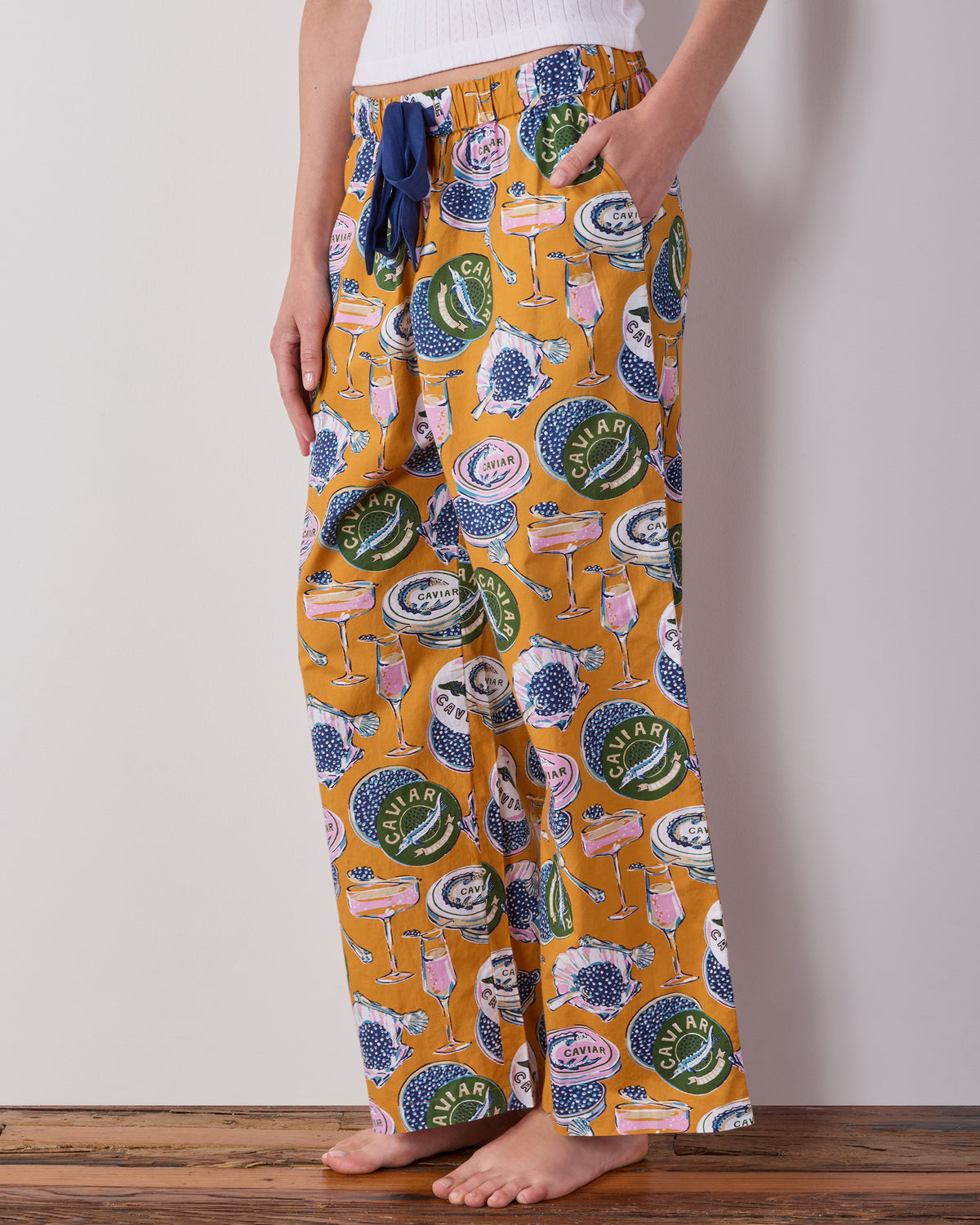 Goldenrod Astrid pajama pants with a Champagne & Caviar print, elastic waistband, and dark blue drawstring, shown on a person.