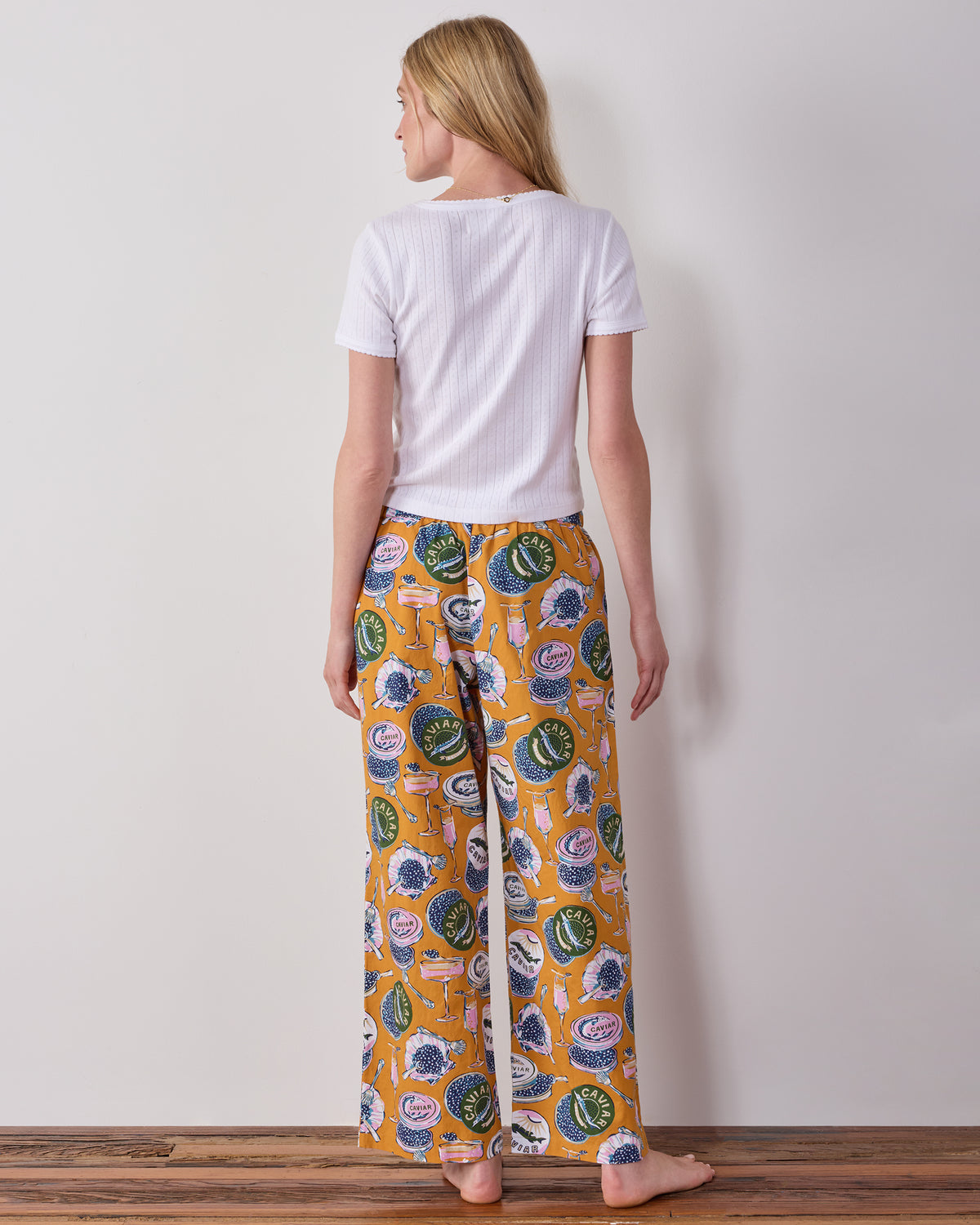 Back view of Goldenrod Petite Astrid pajama pants with a Champagne & Caviar print, shown on a person.
