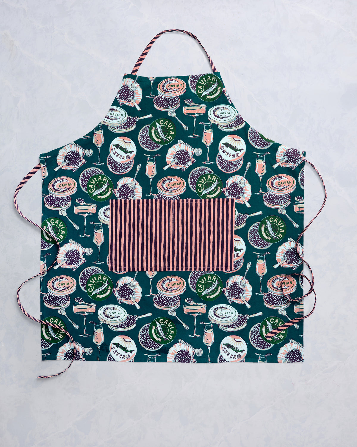Champagne and Caviar apron laid flat, showing its dark teal illustrated pattern, striped ties, and large front pocket.