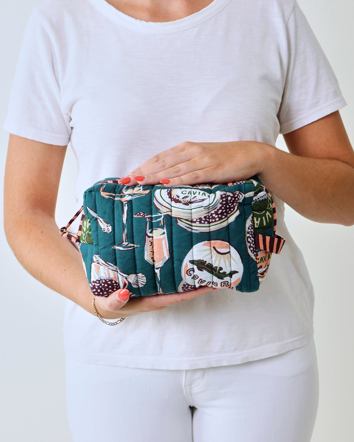 Close-up of a quilted pouch with a dark teal Champagne and Caviar print featuring glasses, tins, and bottles.