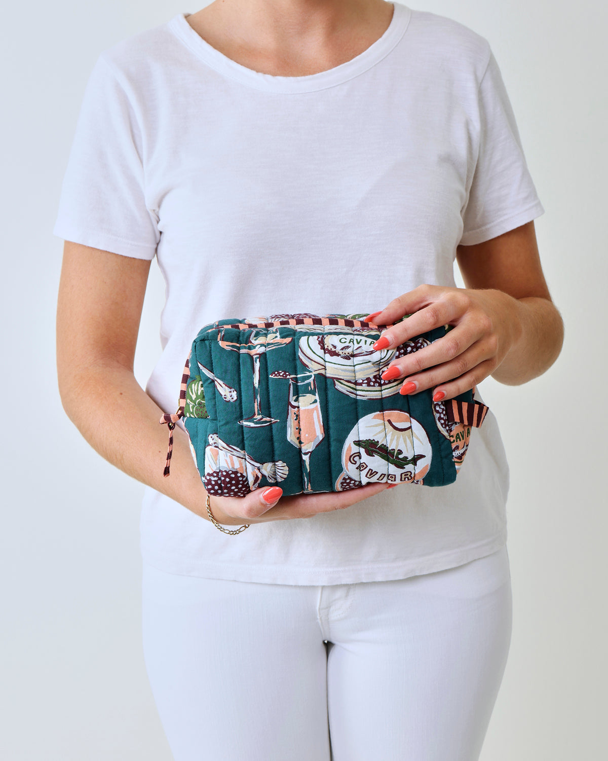 Quilted Champagne & Caviar pouch with a peacock-feather print, held in front of a person wearing a white shirt.