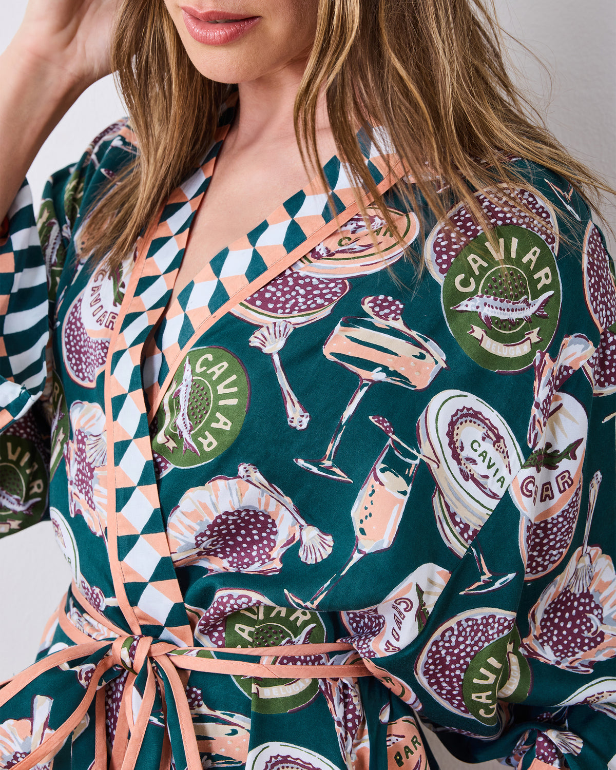 Close-up of the printed wrap robe showing the contrast geometric neckline, waist ties, and caviar-and-champagne motif.