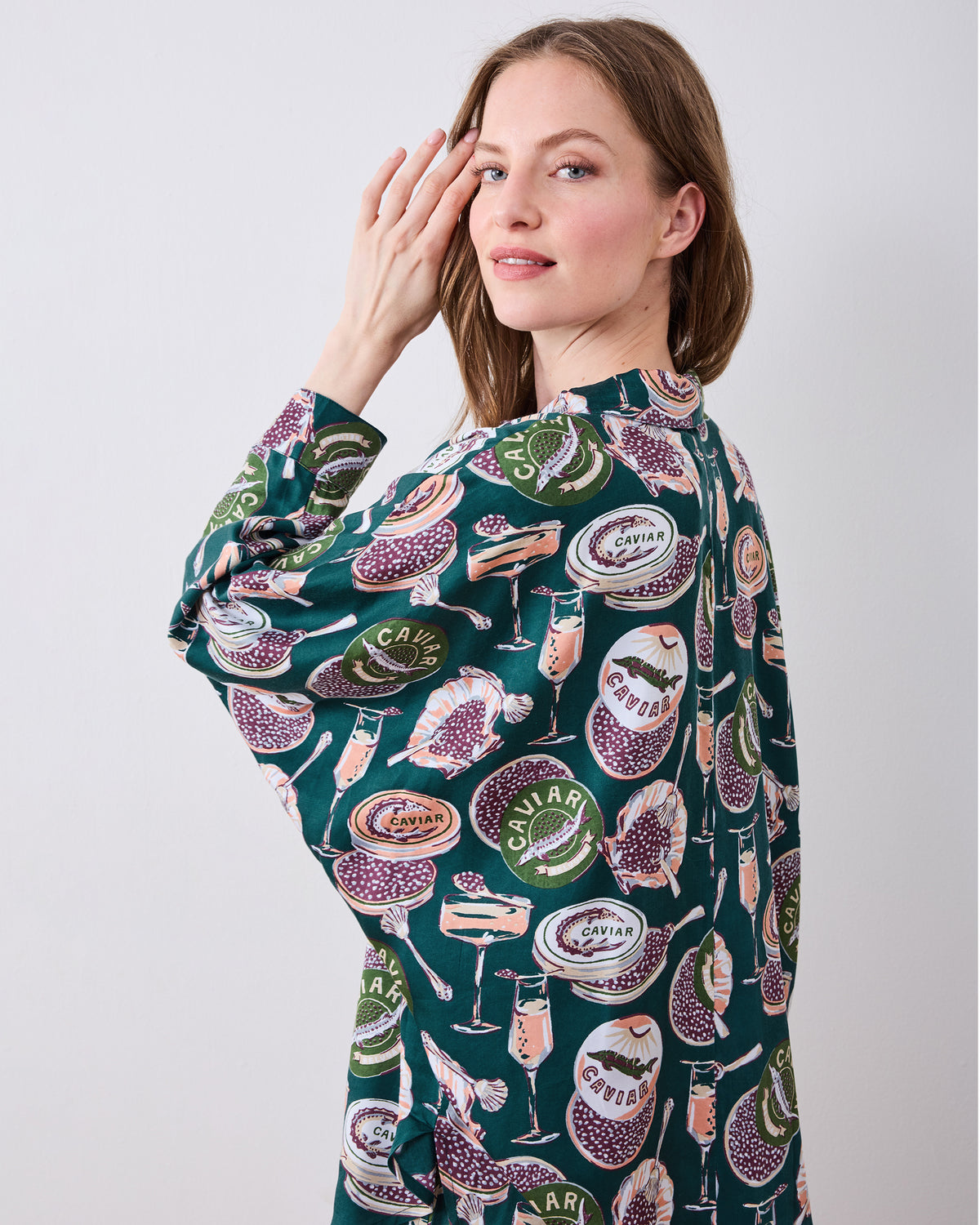 Three-quarter back view of the peacock-feather Champagne & Caviar Stevie pajama top, showing the collar, sleeve, and repeated print.