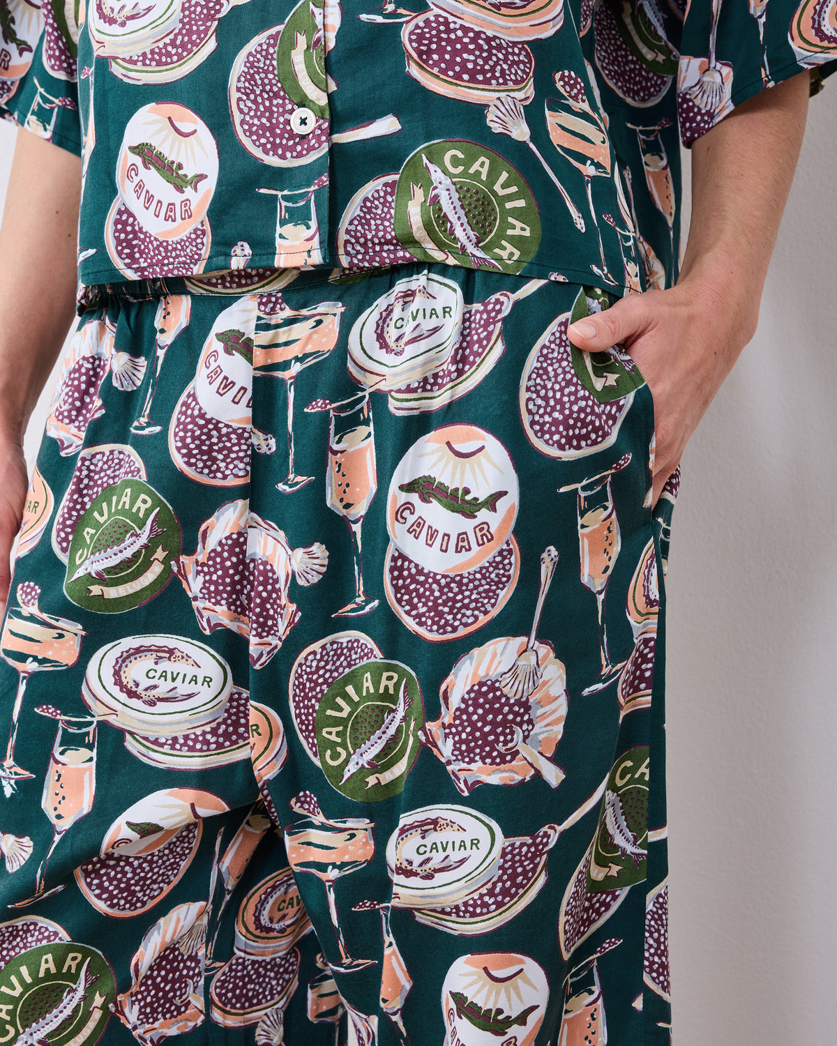 Close-up of the Champagne & Caviar pajama set showing the button-front top hem, elastic waistband, pants pocket, and printed caviar motifs.
