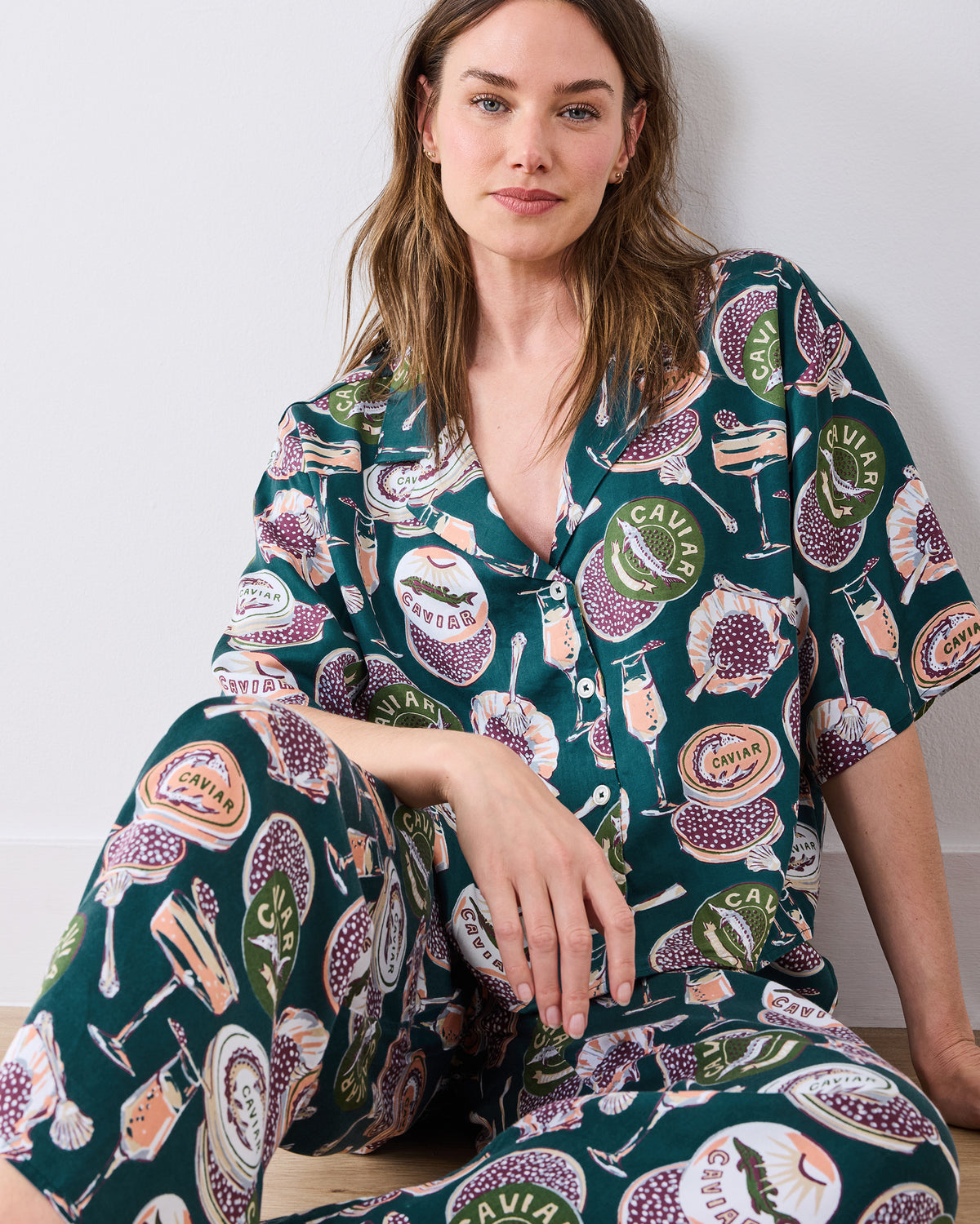 Seated close-up of a person wearing the Champagne & Caviar pajama set, showing the button-front neckline and printed pants.
