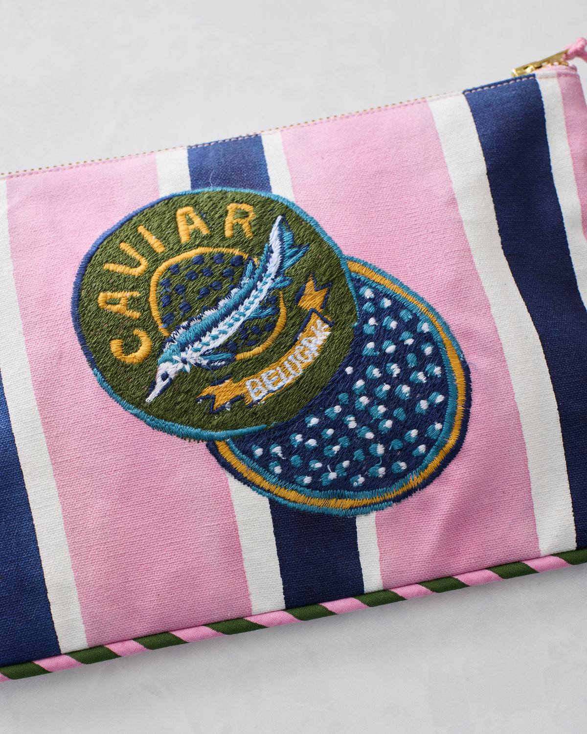 Close-up of the striped canvas pouch’s embroidered CAVIAR patch, showing a fish motif and detailed stitching.