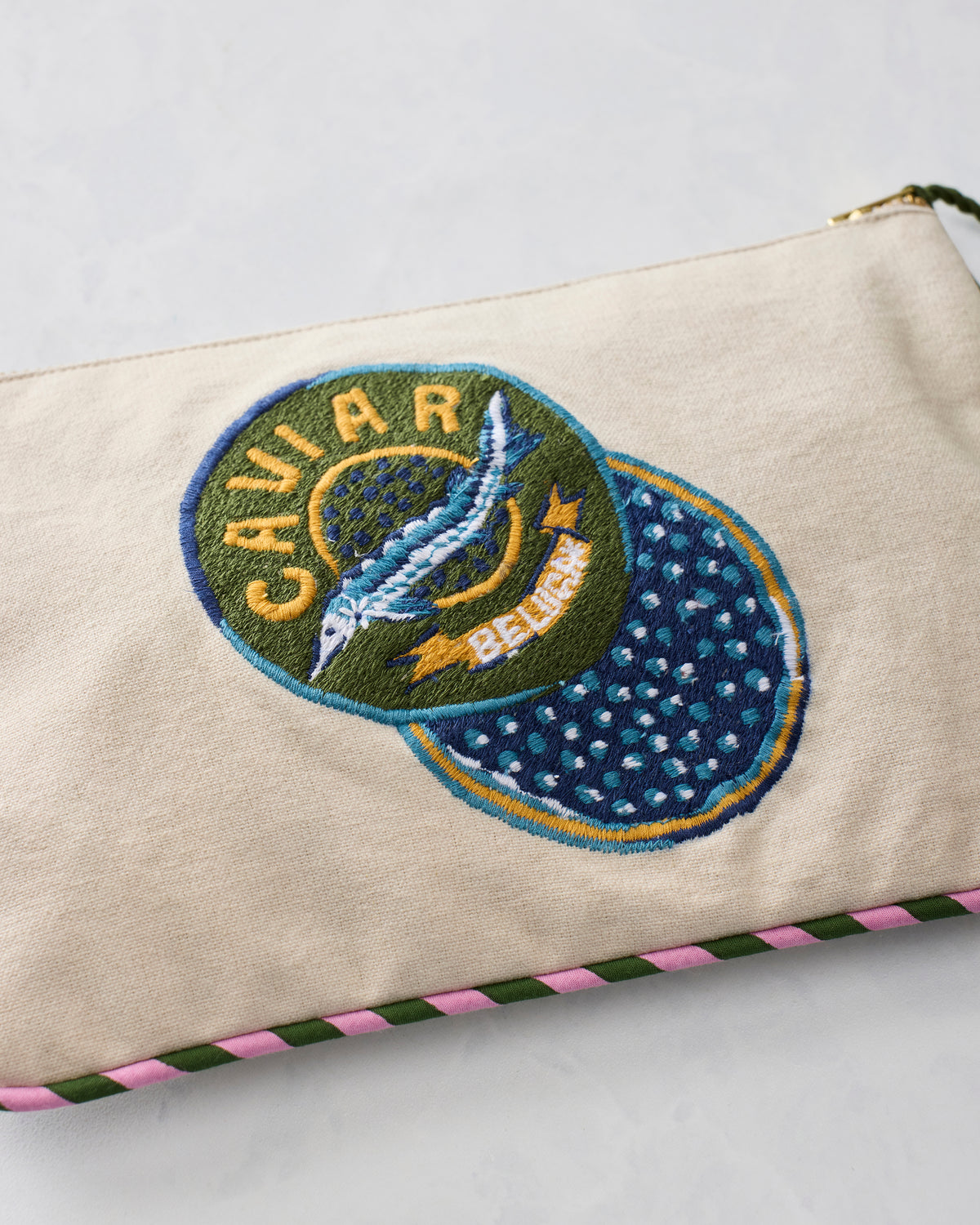 Close-up of embroidered Caviar and Breakfast badge on a natural canvas pouch with pink-and-green trim.