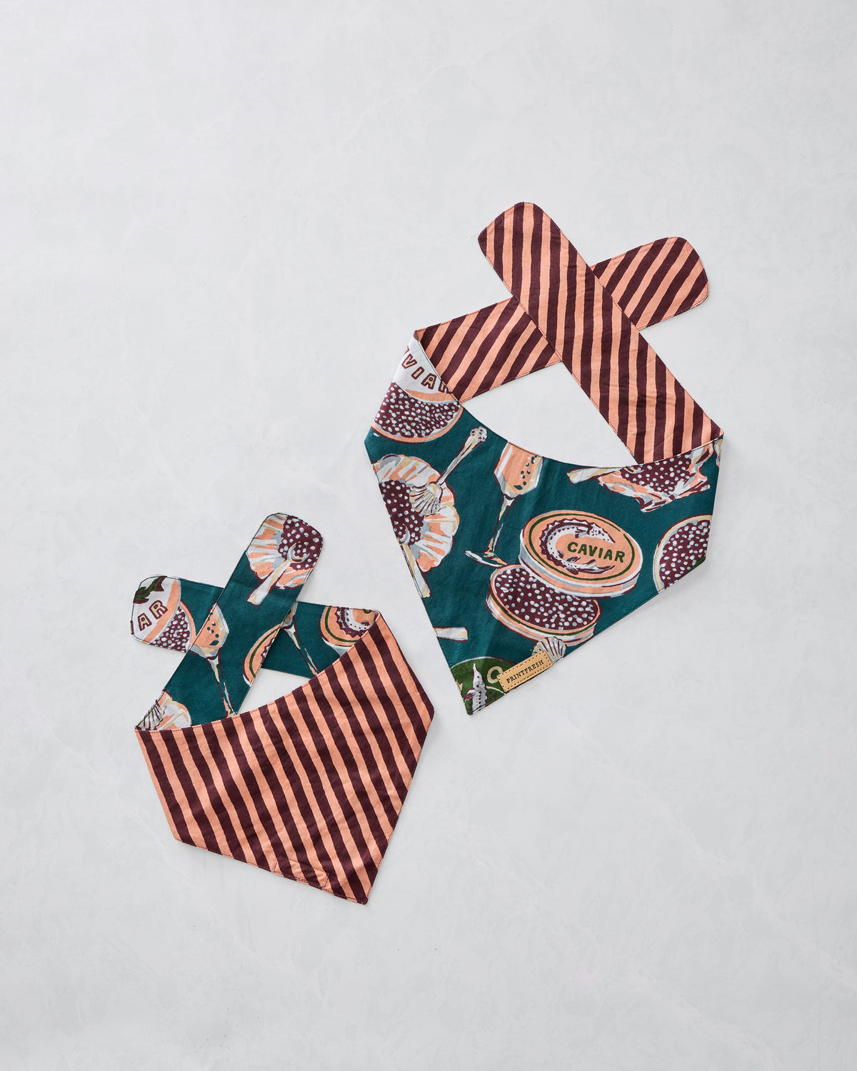 Two Champagne & Caviar pet bandanas displayed flat, showing one printed side and one striped reverse side.