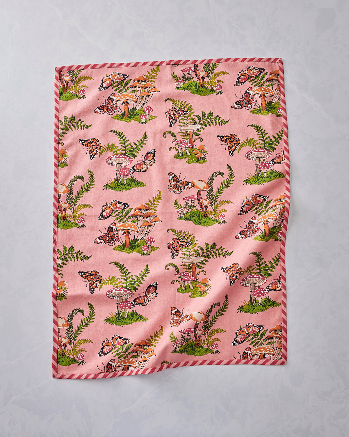 Front view of two pink Butterfly Forager tea towels laid flat, bordered with red-and-white stripes and printed with butterflies, mushrooms, and ferns.