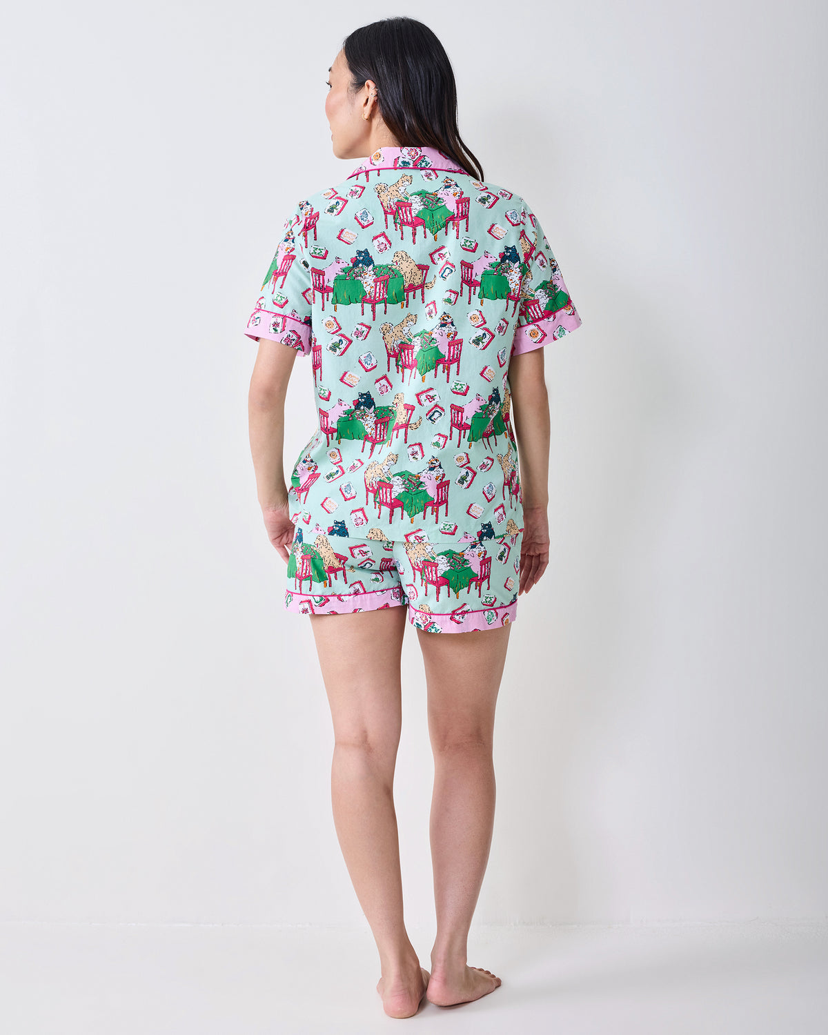 Back view of a model wearing the Mah Jongg Menagerie short pajama set in pale jade, with a button-down top and shorts covered in colorful tile and animal prints.