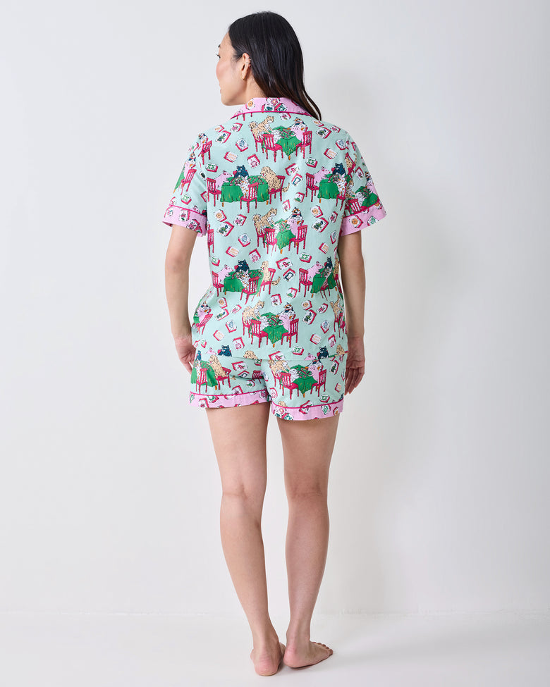 Back view of a model wearing the Mah Jongg Menagerie short pajama set in pale jade, with a button-down top and shorts covered in colorful tile and animal prints.