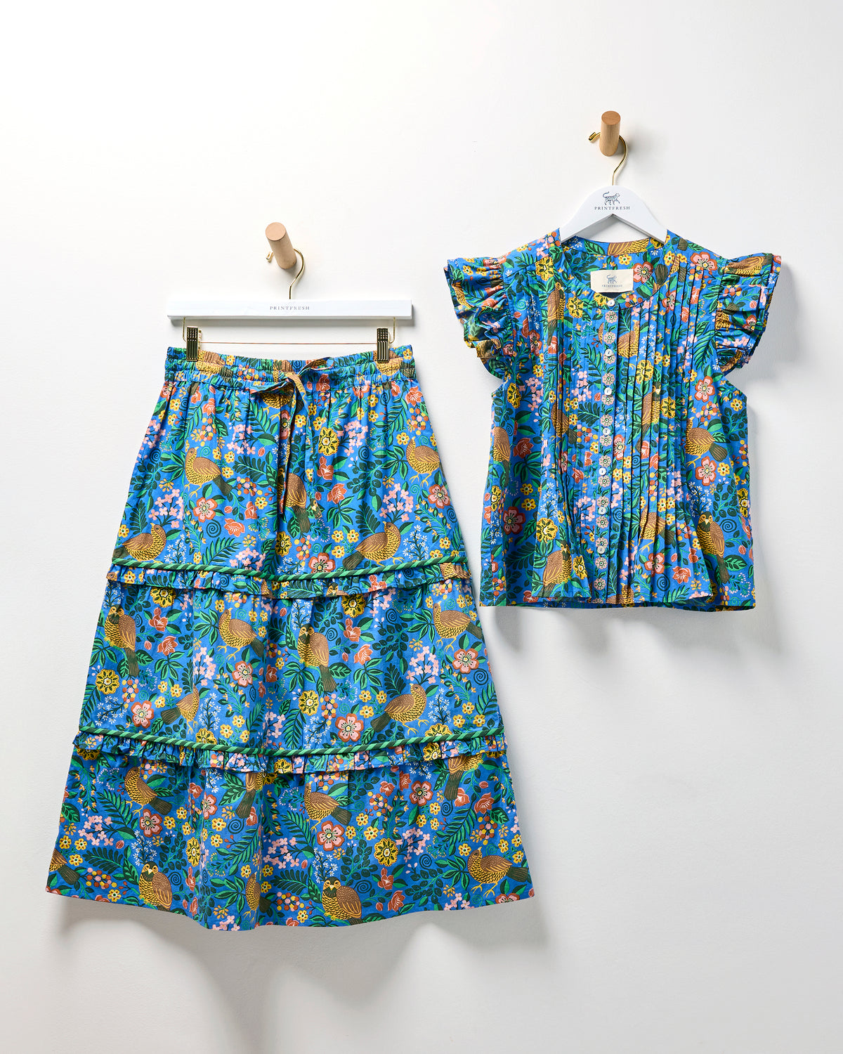 Blue Willow Wren blouse and tiered midi skirt displayed together, with flutter sleeves, gathered details, and a bird-and-floral print.