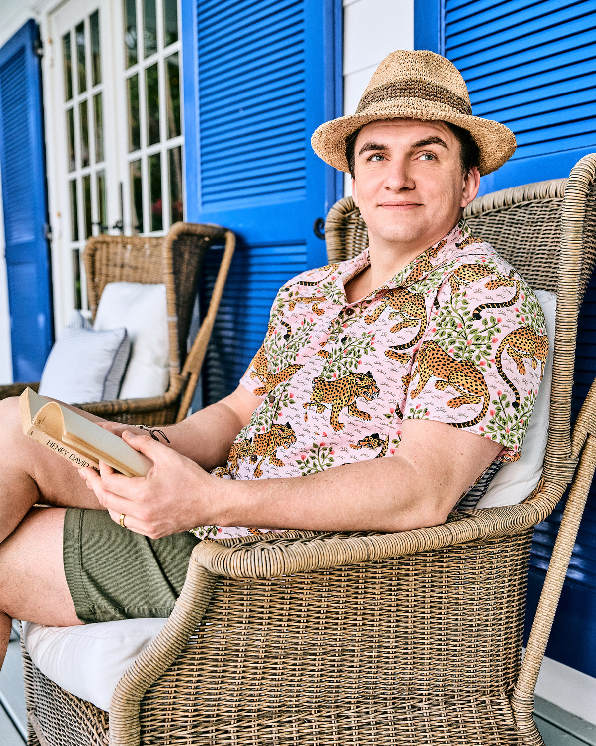 Person wearing the blush Bagheera leopard-print short-sleeve shirt while seated in a wicker chair outdoors.