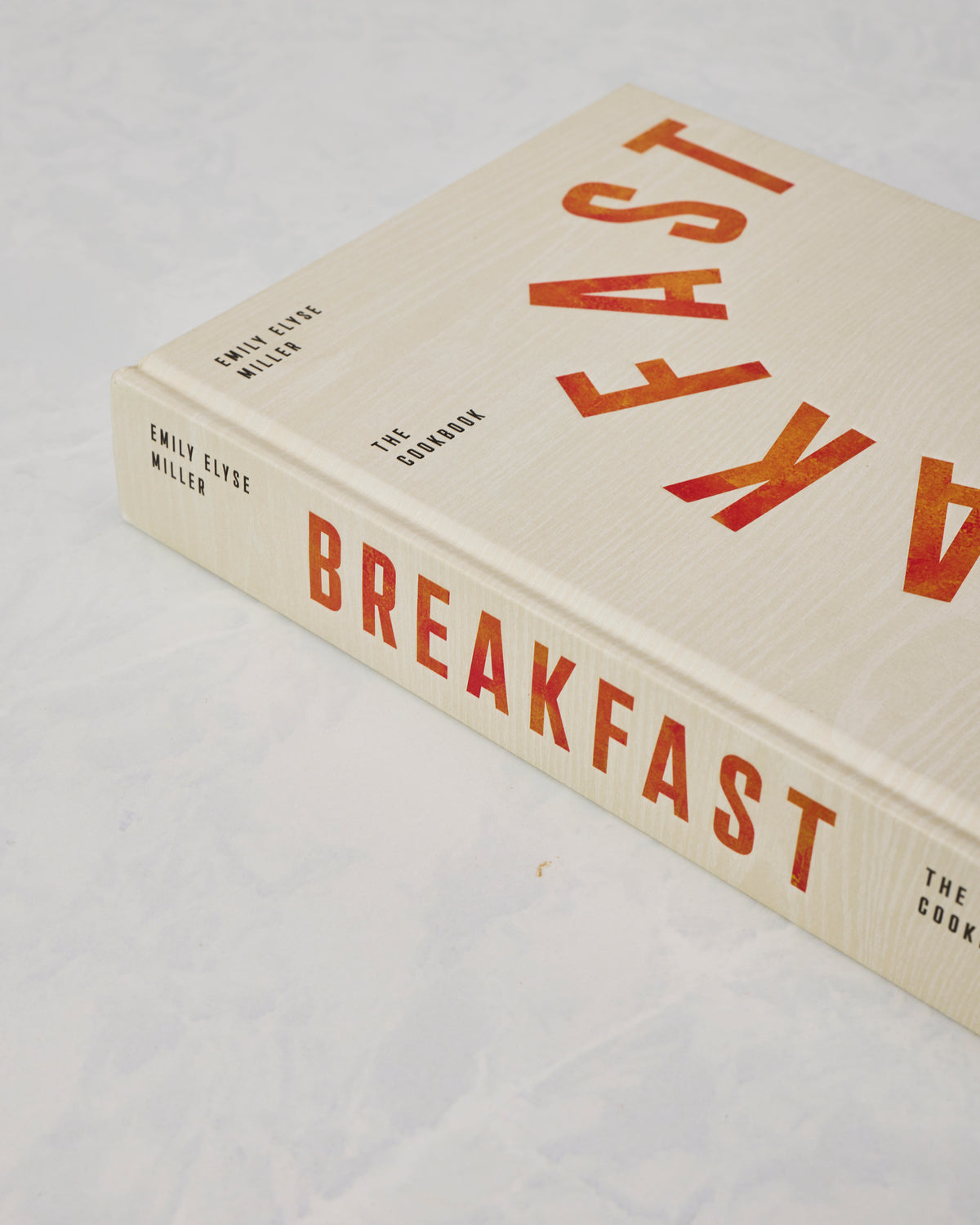 Angled view of the ivory Breakfast: The Cookbook by Emily Elyse Miller, showing the title on the cover and spine.