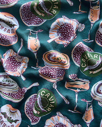 Dark teal patterned fabric with caviar tins, spoons, and cocktail glasses