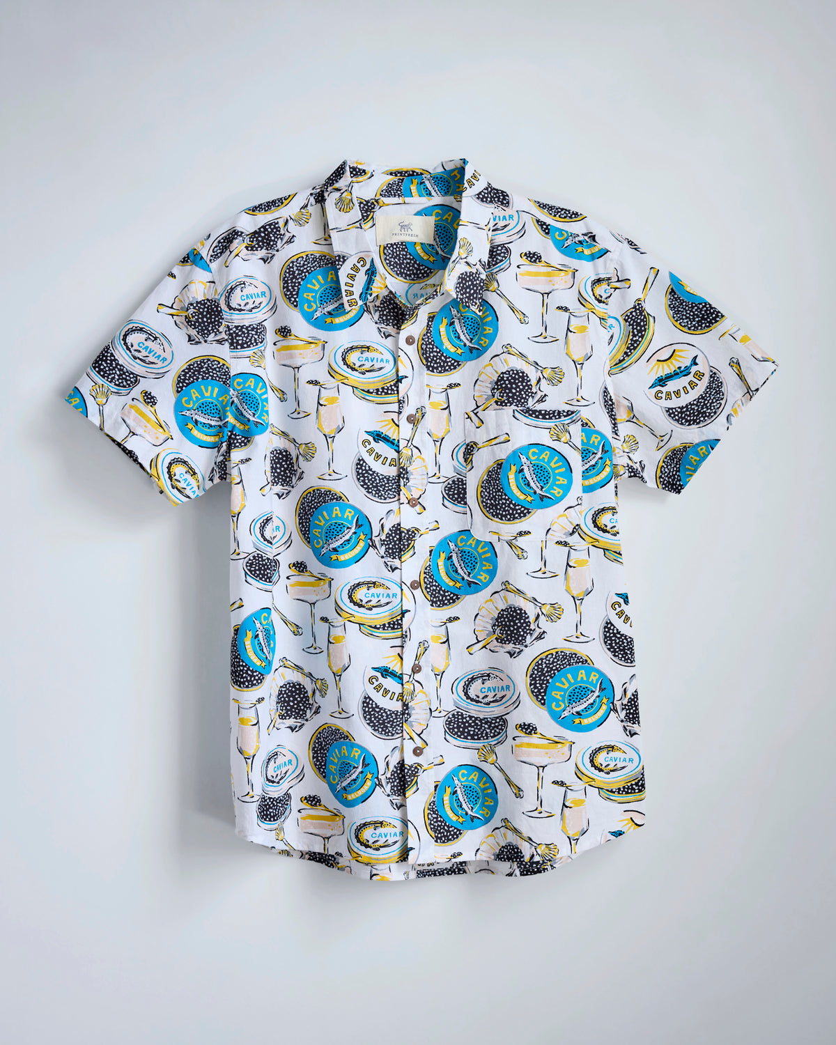 Flat-lay of the Cloud Champagne & Caviar Leo Shirt with a caviar-and-champagne print, short sleeves, collar, chest pocket, and button front.