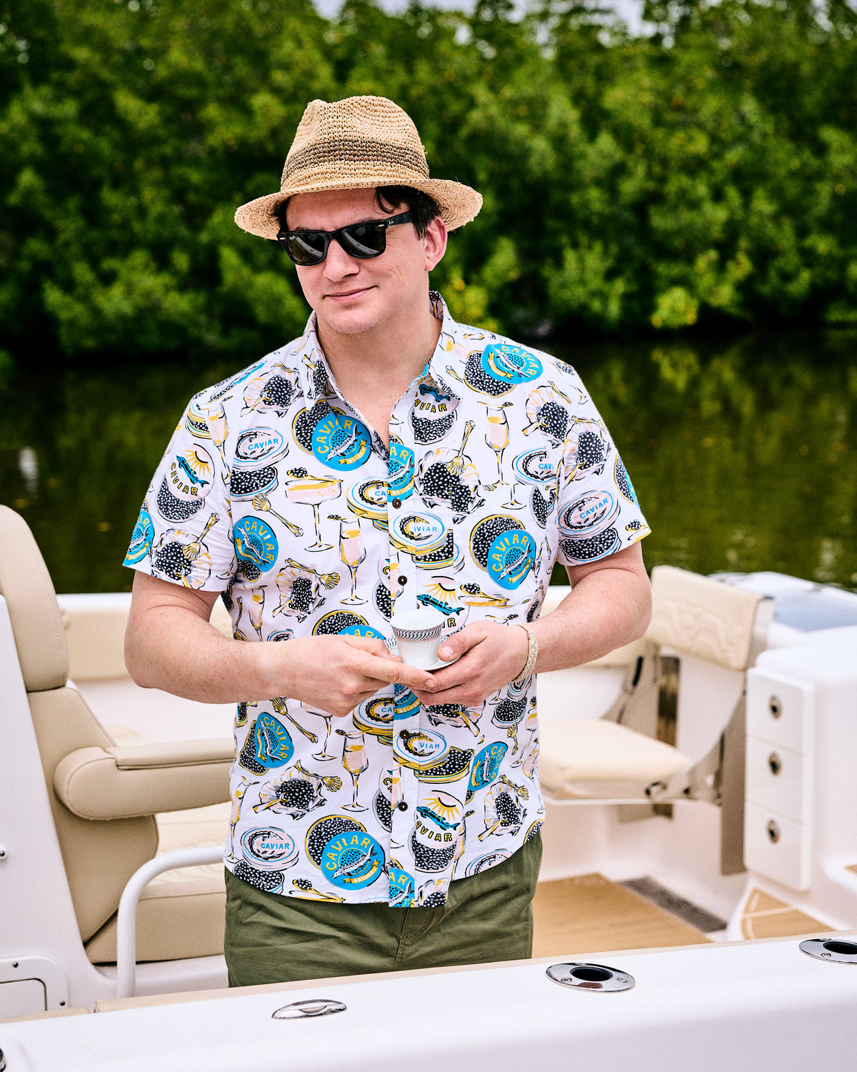 Front view of the Champagne & Caviar Leo Shirt worn on a boat, showing the button front, chest pocket, and printed caviar and champagne pattern.