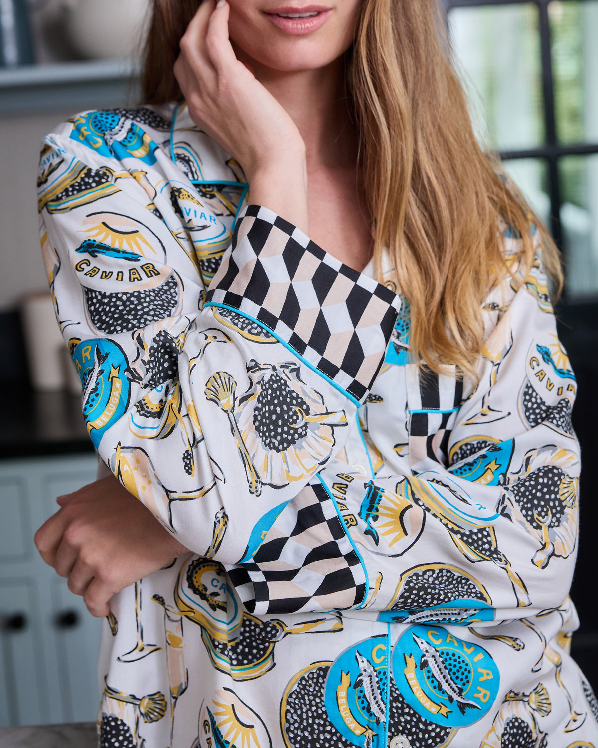 Close-up of the Pearl Champagne & Caviar pajama top, highlighting the printed front, piping, buttons, and black-and-white checkered cuff and pocket.