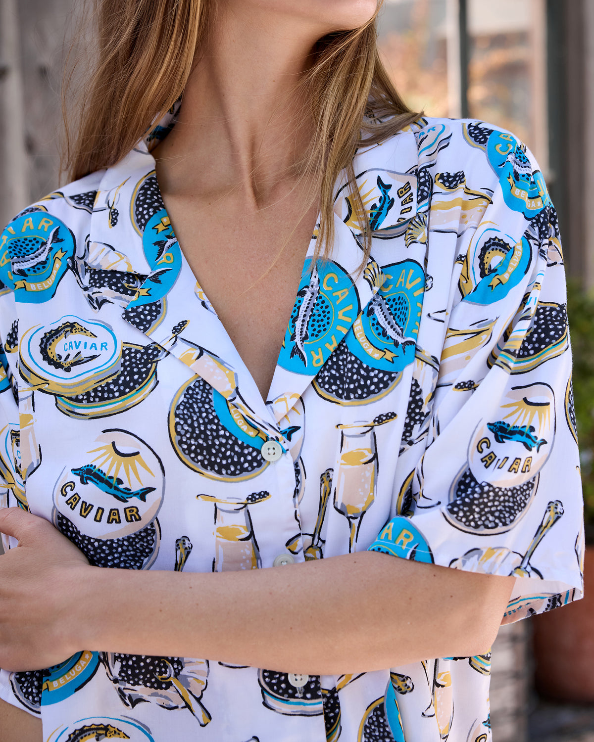 Close-up of the pajama top showing its notched collar, white buttons, and champagne glass and caviar tin print.