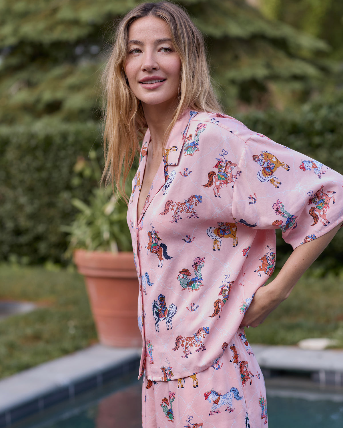 Three-quarter view of a model wearing the pink cowgirl-print pajama top and matching pants outdoors.