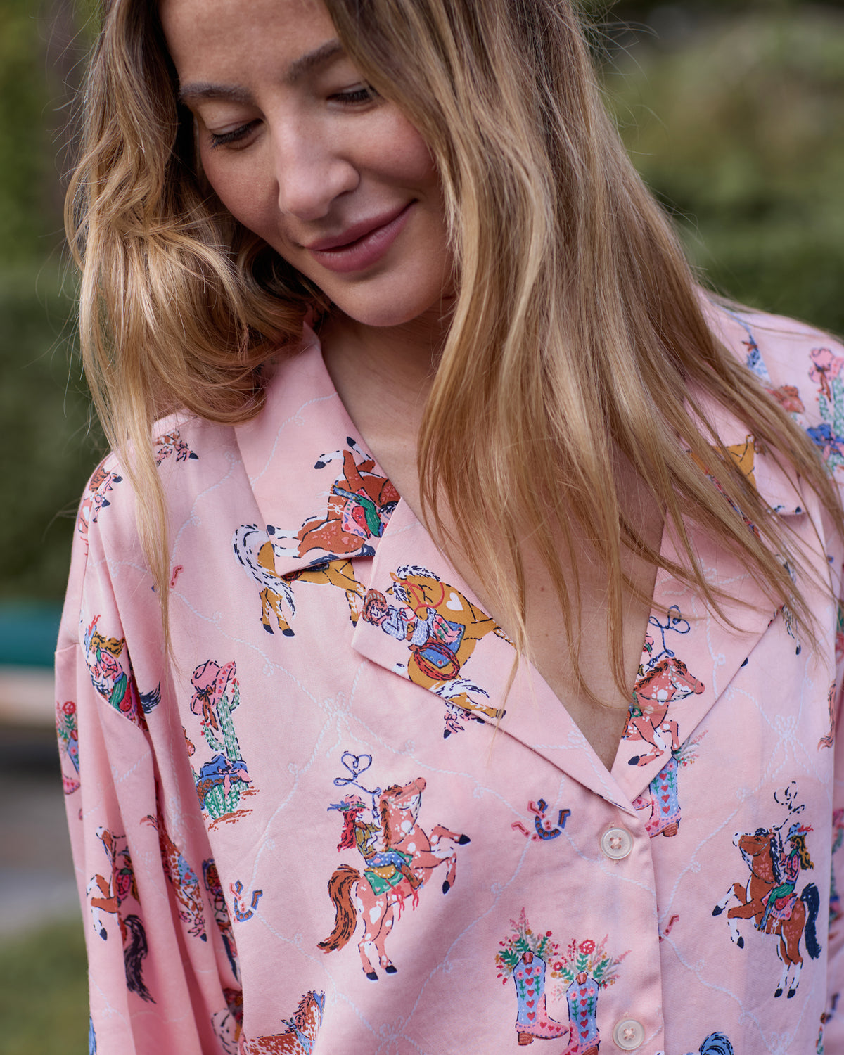 Close-up of the pink long pajama top with a notched collar, front buttons, and horse-and-cowgirl print.