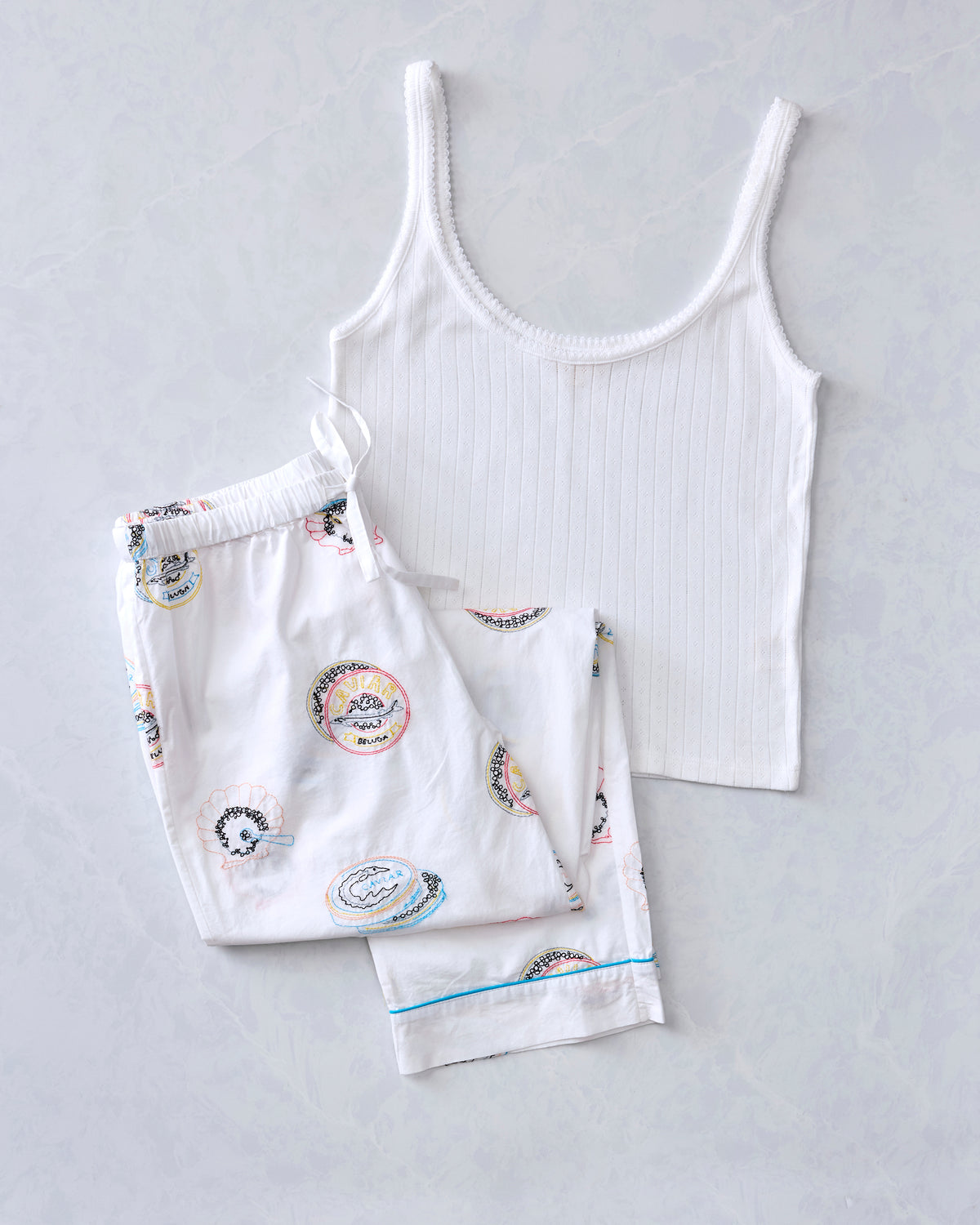 Flat lay of white ribbed tank top and matching printed pajama pants from the Embroidered Caviar Club bundle.