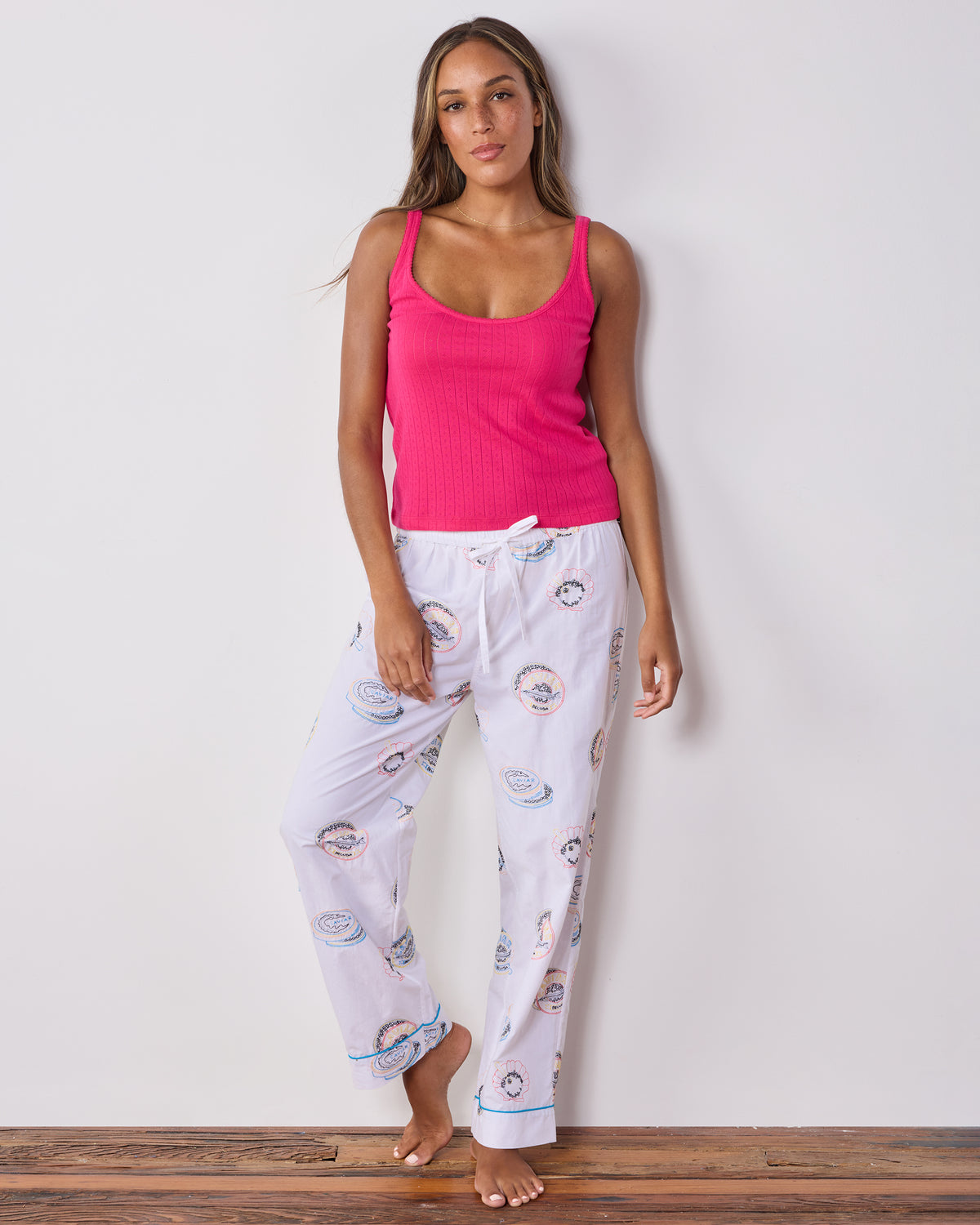 Front view of pearl pajama pants with embroidered caviar tin motifs, shown with a pink tank top.