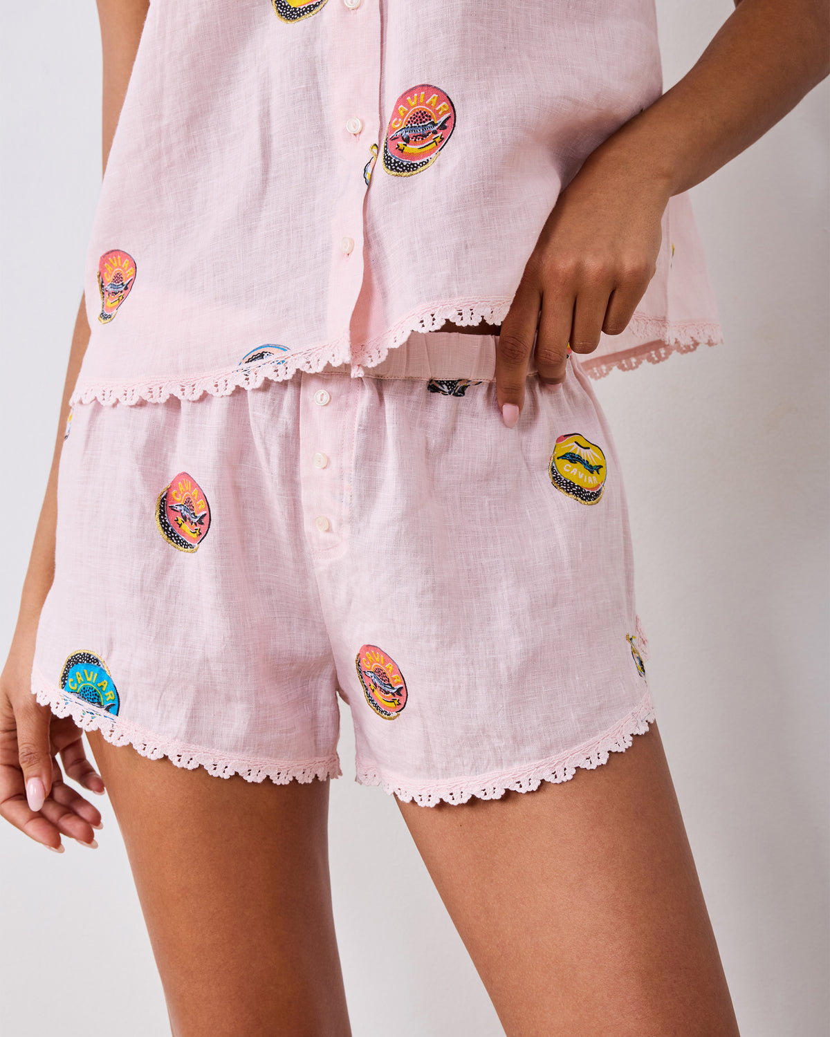 Close-up of the Pink Pearl shorts showing the elastic waistband, front buttons, embroidered caviar tin motifs, and scalloped trim.